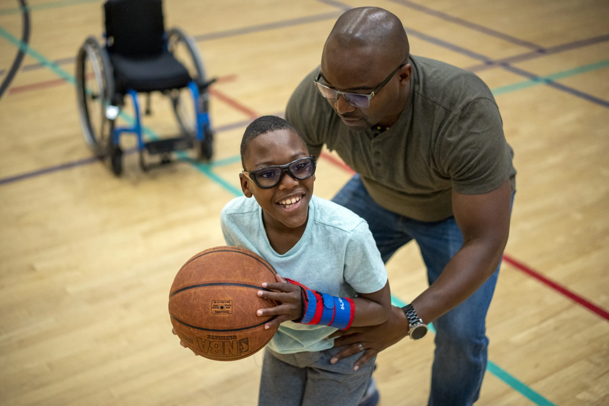 A child with an arm brace holds a basketball, supported by an adult.