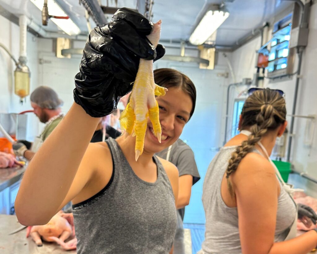 Youth holding a chicken foot in Makoce's Mobile Poultry Processing Unit