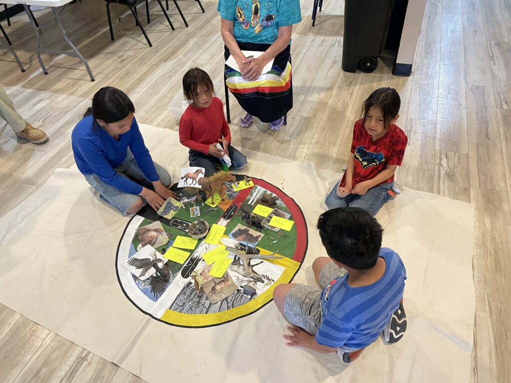 Children gather around a traditional learning activity with a Lakota elder.