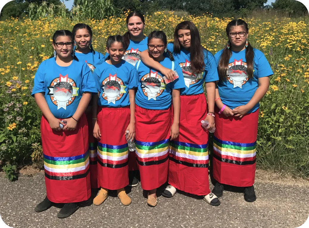 A group of youth standing in red skirts with black, green, white, and yellow stripes.