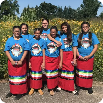 A group of youth standing in red skirts with black, green, white, and yellow stripes.