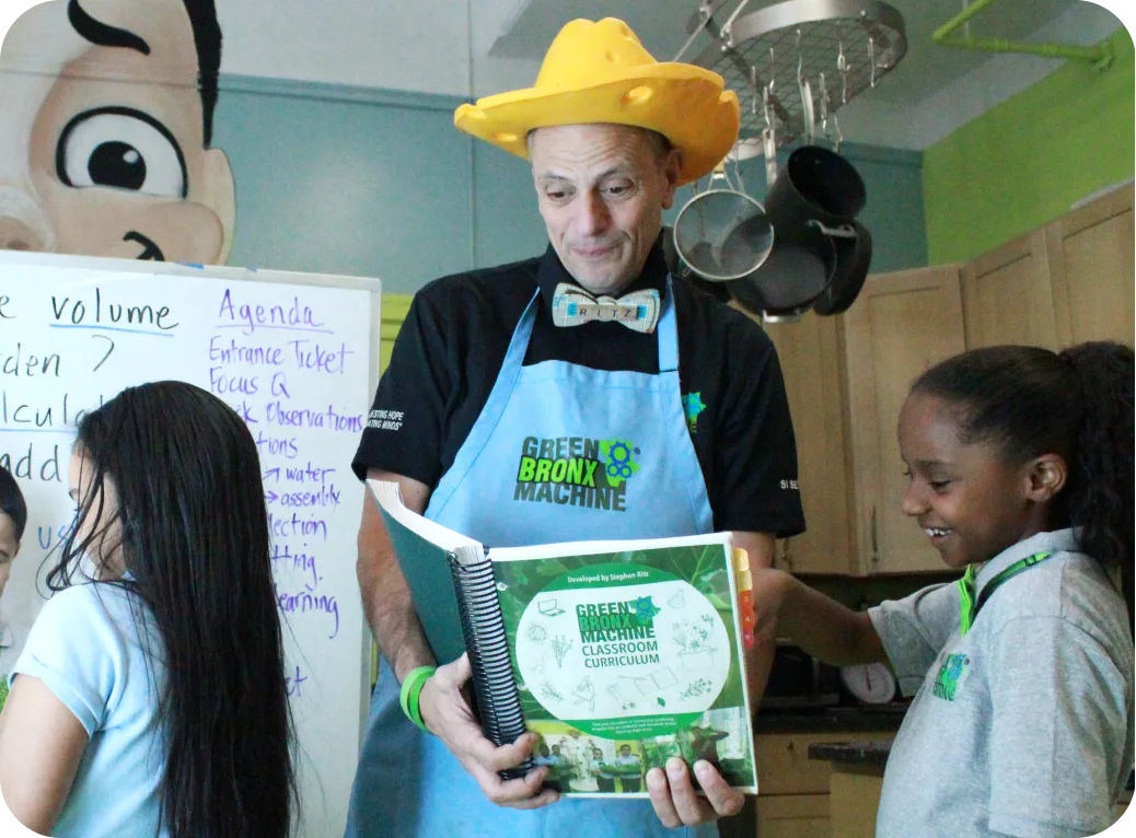 Stephen Ritz in his cheese hat shares information with a young student.
