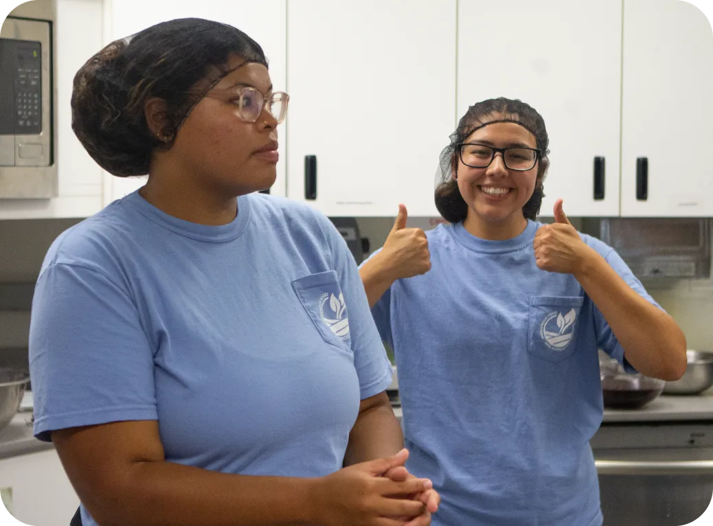 A teenager wearing a hairnet gives a thumbs up in a classroom.