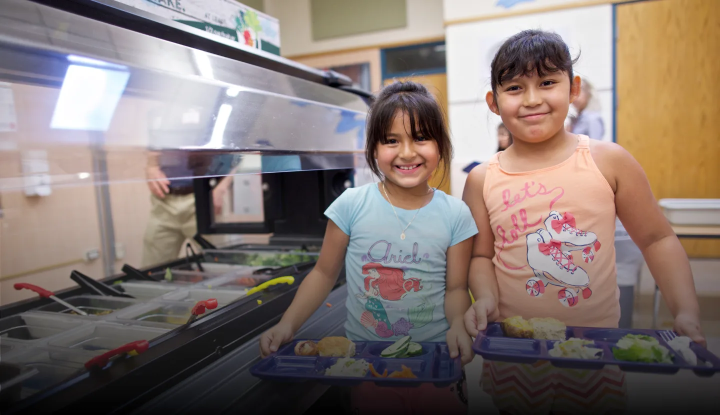 Two girls stand at lunch salad bar, smiling