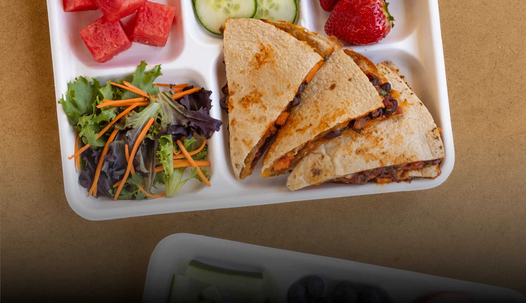 Vibrant and colorful school lunch trays with fruit, veggies, quesadillas, and chickpeas.