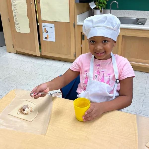A young person in a chef hat at a table.